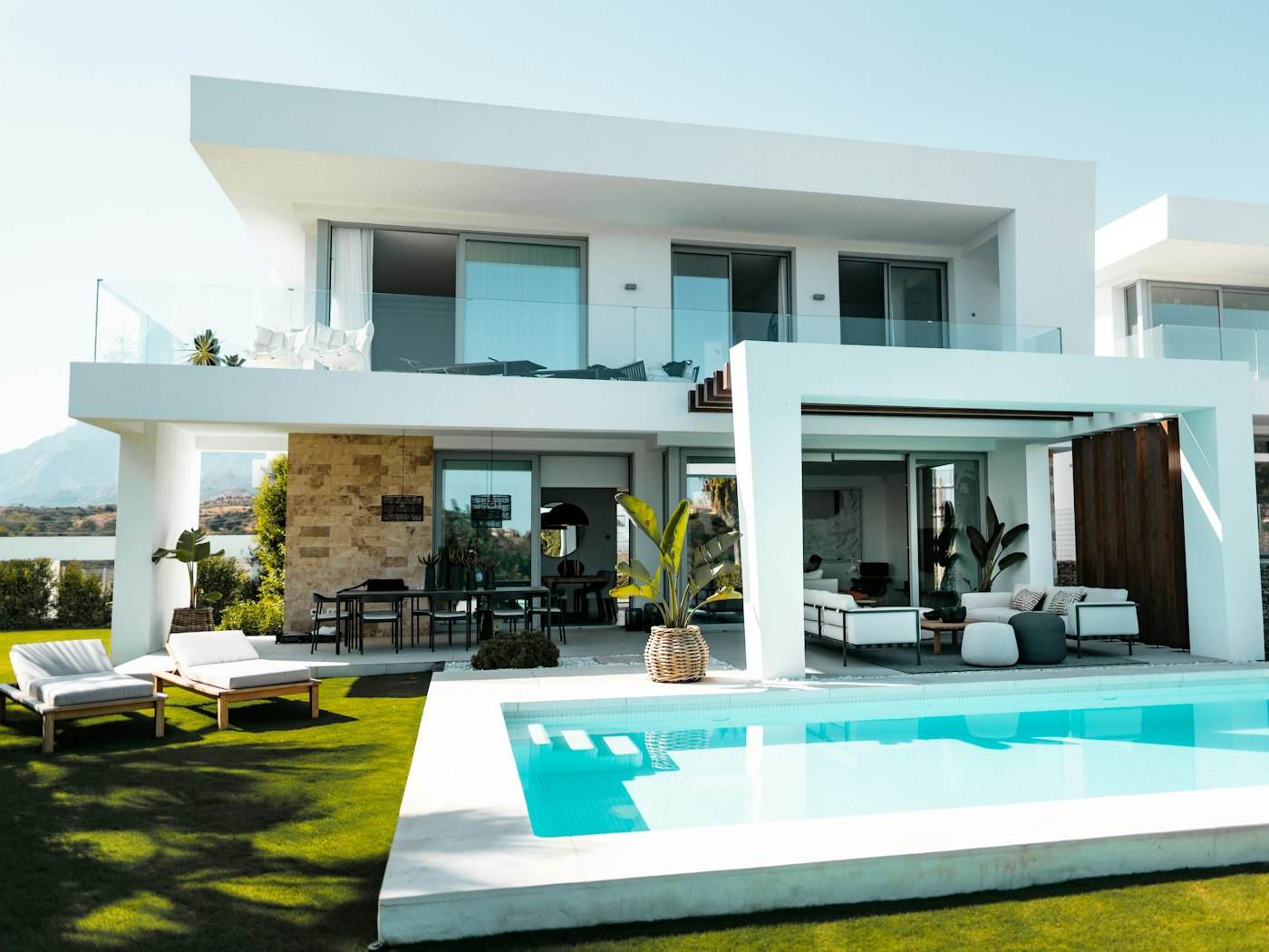 New white modern two-story home with a pool, glass railings, and palms