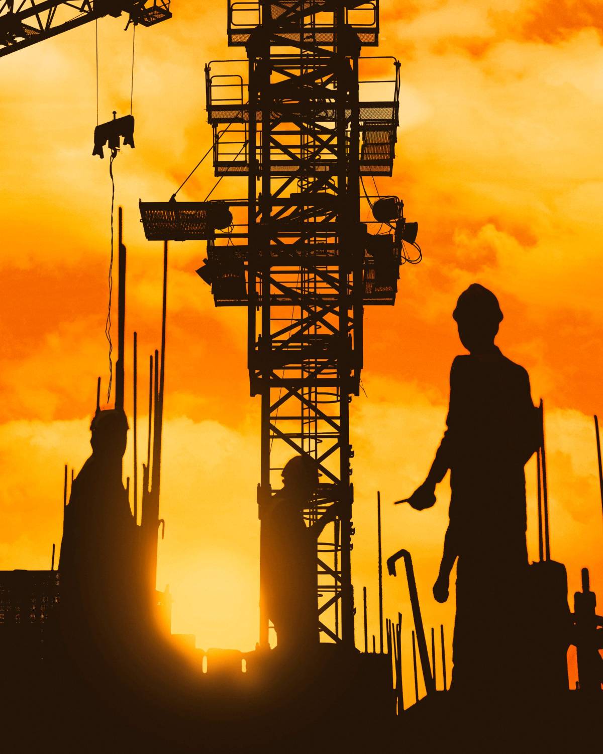 Silhouette of a foreman under a tower crane on a job site at sunset