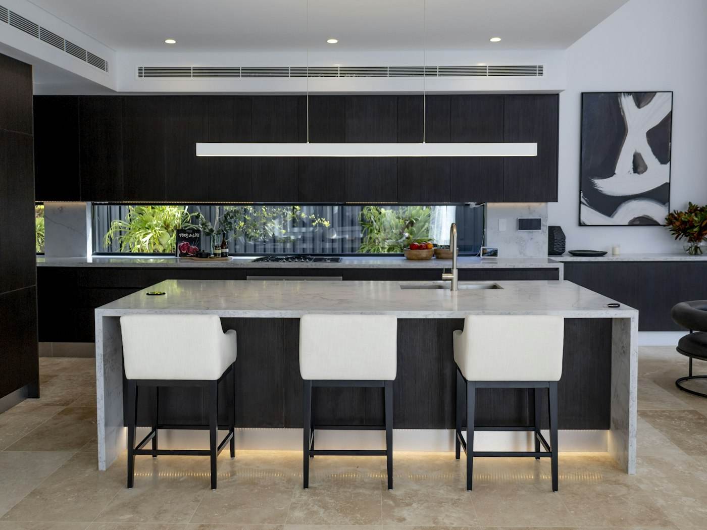 Modern kitchen with black cabinetry, a marble waterfall island lit from below, and a linear pendant